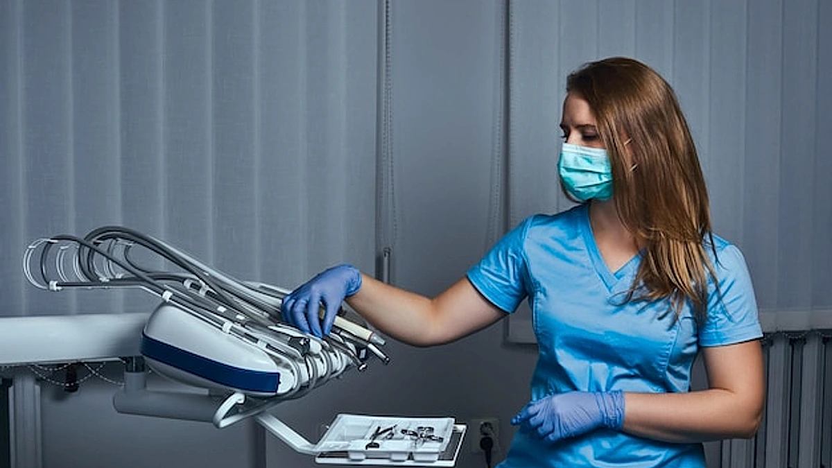 Female dentist wearing a uniform and mask sitting on a chair at his workplace in a dental clinic.